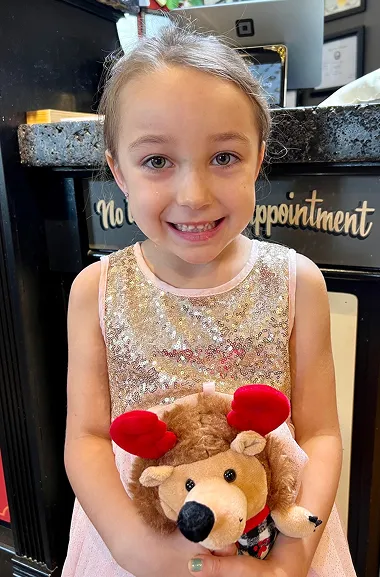 A smiling child holding a plush teddy bear wearing red ears
